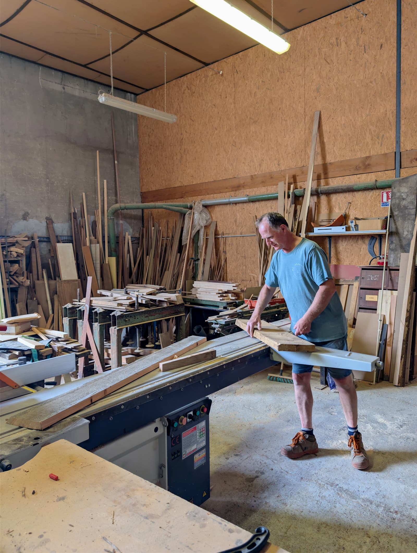 Le menuisier de l'atelier Saint-Georges portant une planche près de la scie à format